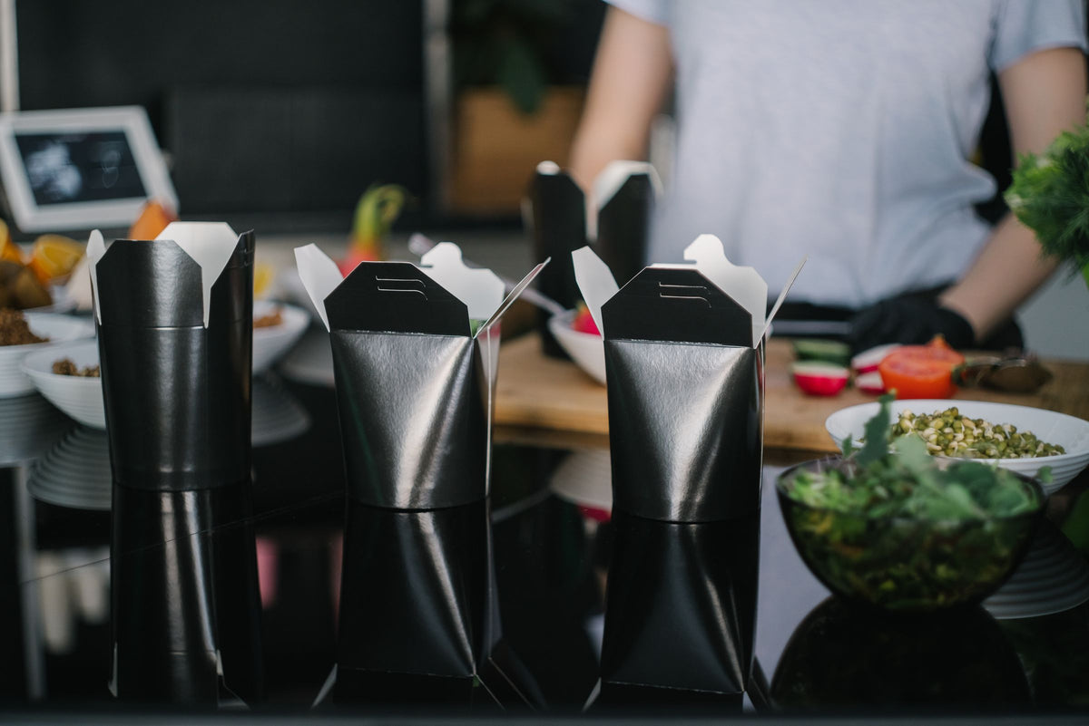 Emballages de livraison noirs alignés sur le comptoir d'une cuisine professionnelle.