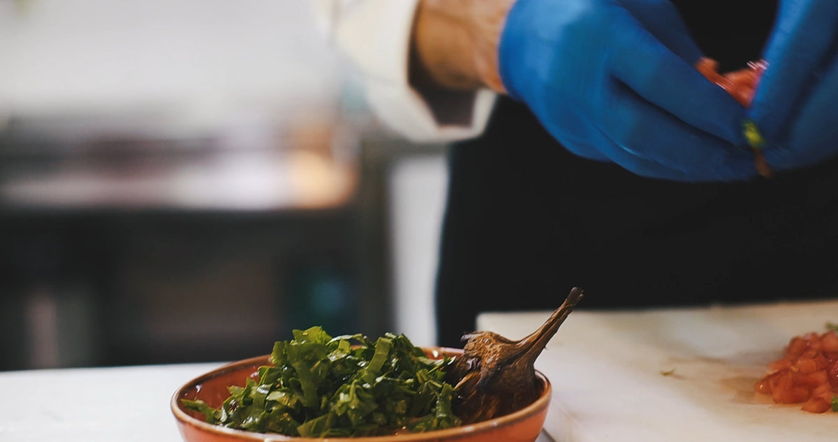 Mains gantées dressant une assiette dans une cuisine professionnelle, sans visage
