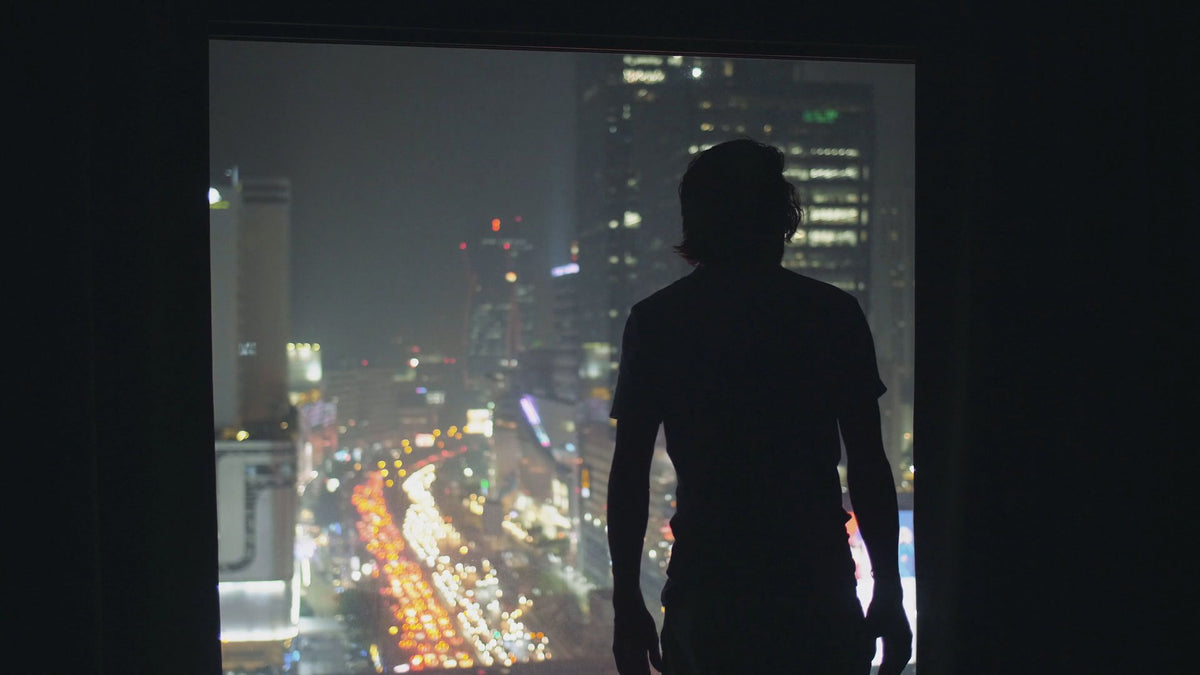 Silhouette d'une personne devant une baie vitrée, la ville de nuit en contrebas.