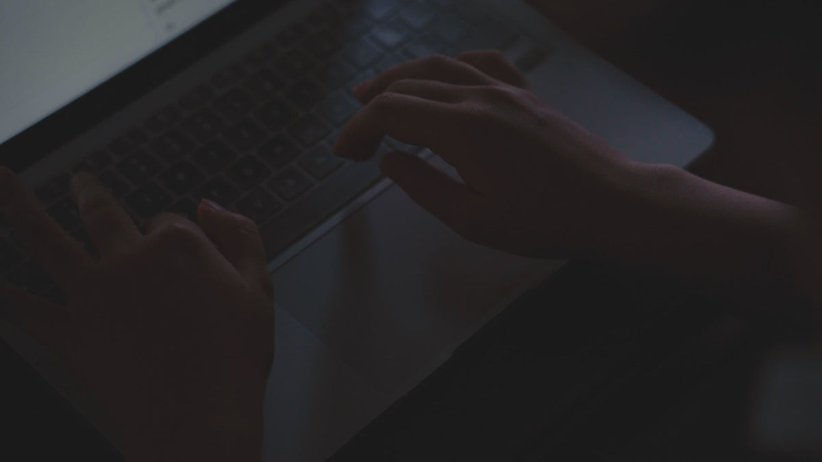 Mains tapant sur le clavier d'un ordinateur portable dans une pièce sombre.